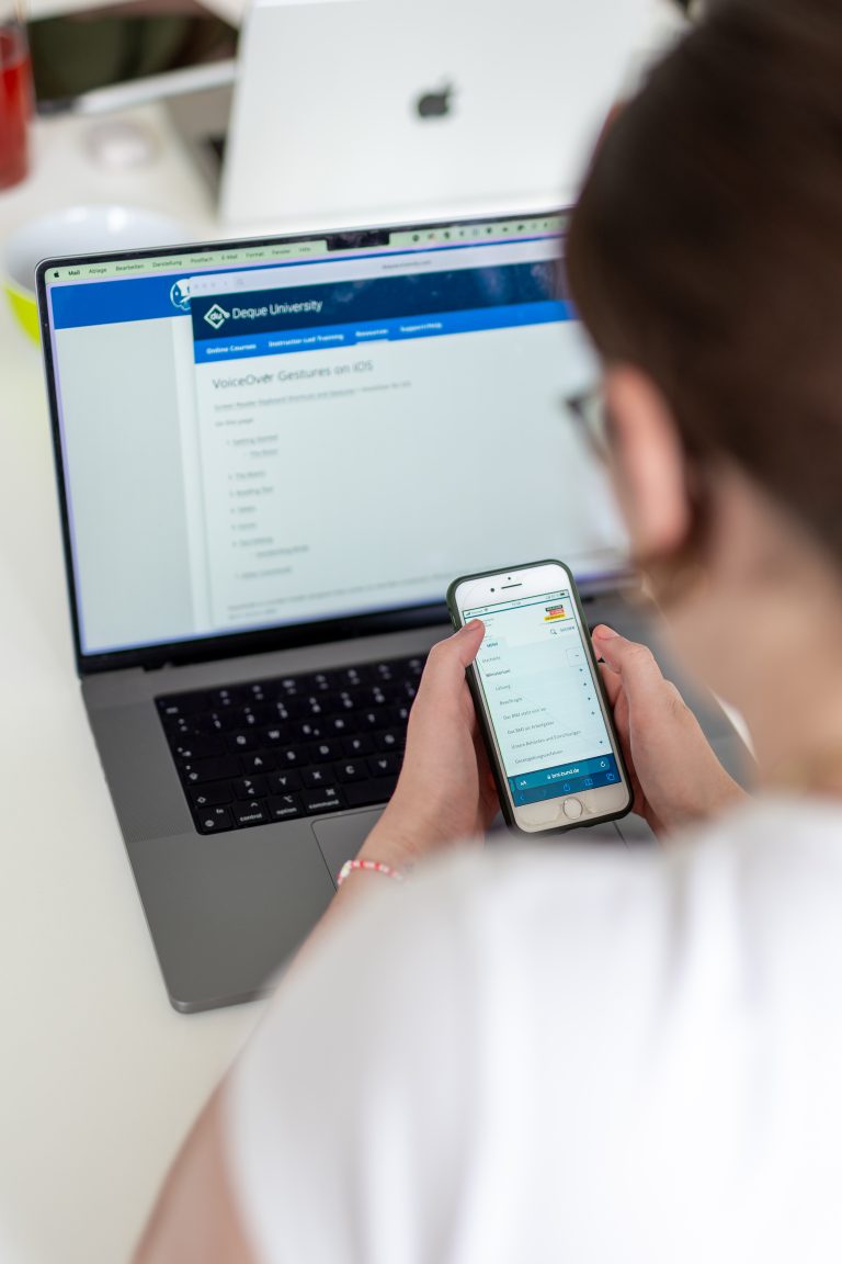 Person nutzt Smartphone und Laptop gleichzeitig, auf dem Laptop ist eine Lernplattform mit dem Titel ‚Oracle University‘ geöffnet. Das Smartphone zeigt eine Liste von Aufgaben oder Inhalten.